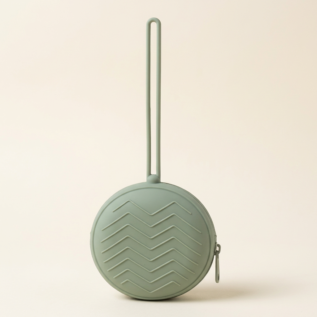 Single sage-green round pacifier travel case with chevron texture, zipper and full hanging loop on warm ivory