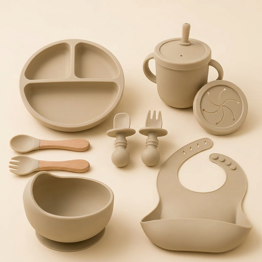 Single beige silicone feeding set with divided plate, suction bowl, bib, handled straw cup, snack lid and two utensil pairs on warm ivory