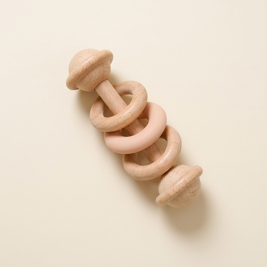 Single beech wood baby rattle with two wooden rings and a soft-peach silicone ring on warm ivory